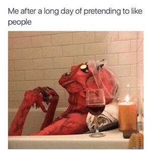 A red demon costume figure relaxes in a bathtub with a wine glass, candle, and towel; overlaid text reads, "Me after a long day of pretending to like people."